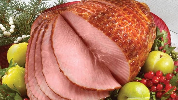 sliced ham on a platter surrounded by fruit and greenery, with pine cones in the background