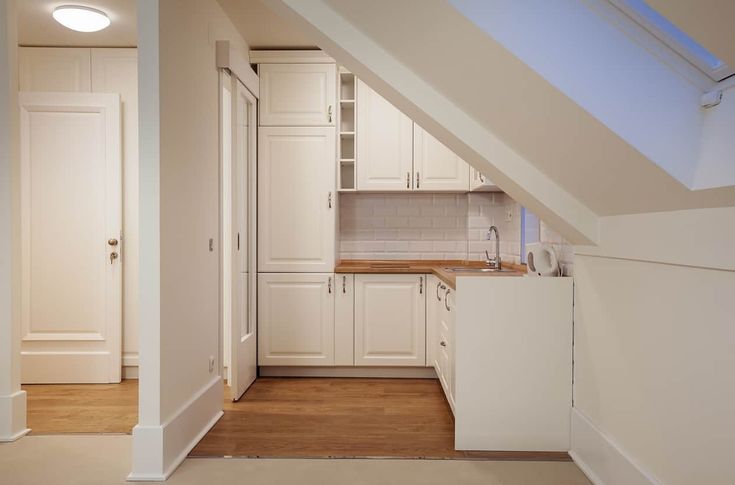 an attic kitchen with white cabinets and wood floors