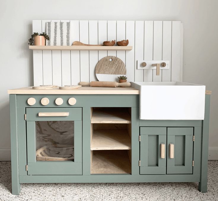 a green wooden play kitchen with sink and cupboards