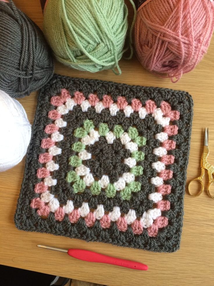 crocheted granny square with yarn and scissors on the table next to it is a ball of yarn