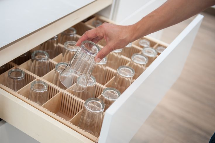 a person holding a bottle in an open drawer filled with empty wine glasses and drinking glasses