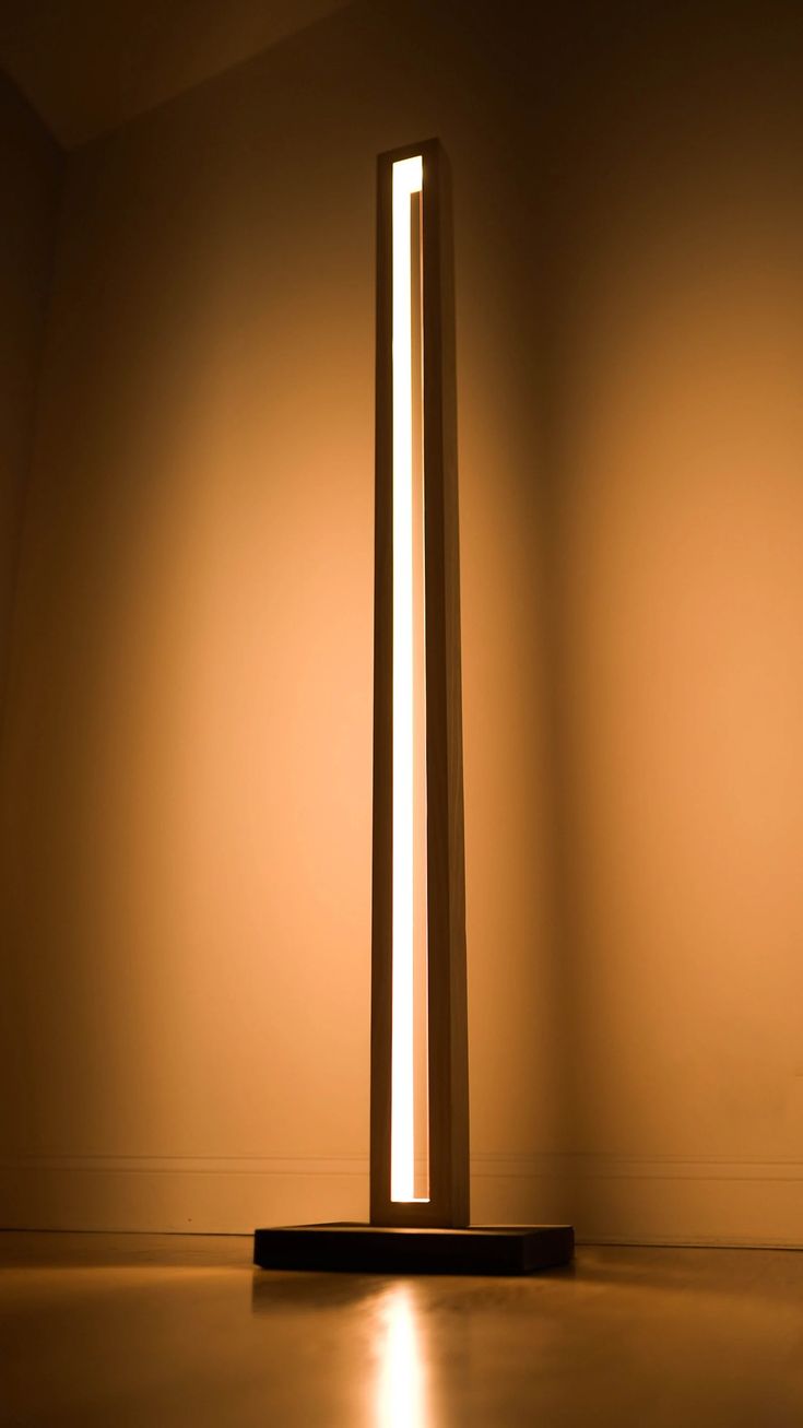 a tall light sitting on top of a wooden floor next to a white wall in an empty room