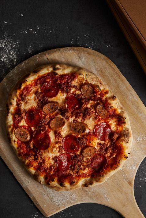 a pepperoni pizza sitting on top of a wooden cutting board next to a box