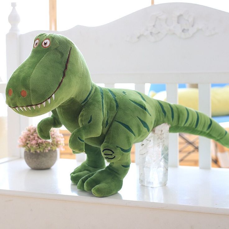 a stuffed toy dinosaur sitting on top of a white table next to a potted plant