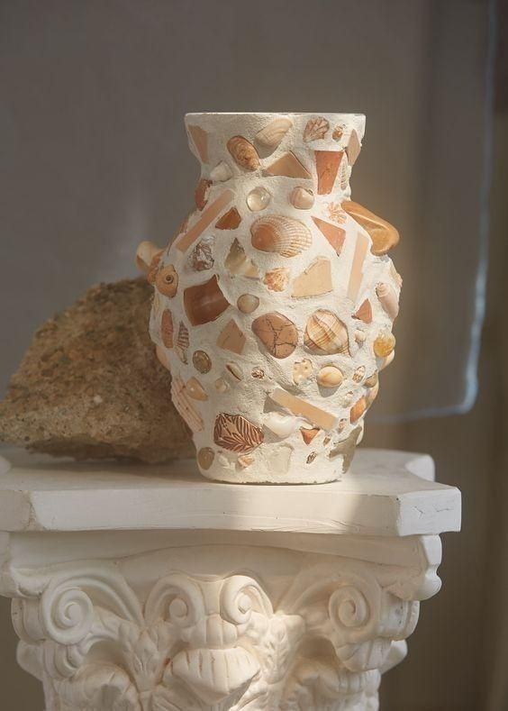 a white vase sitting on top of a table next to a piece of bread and a rock