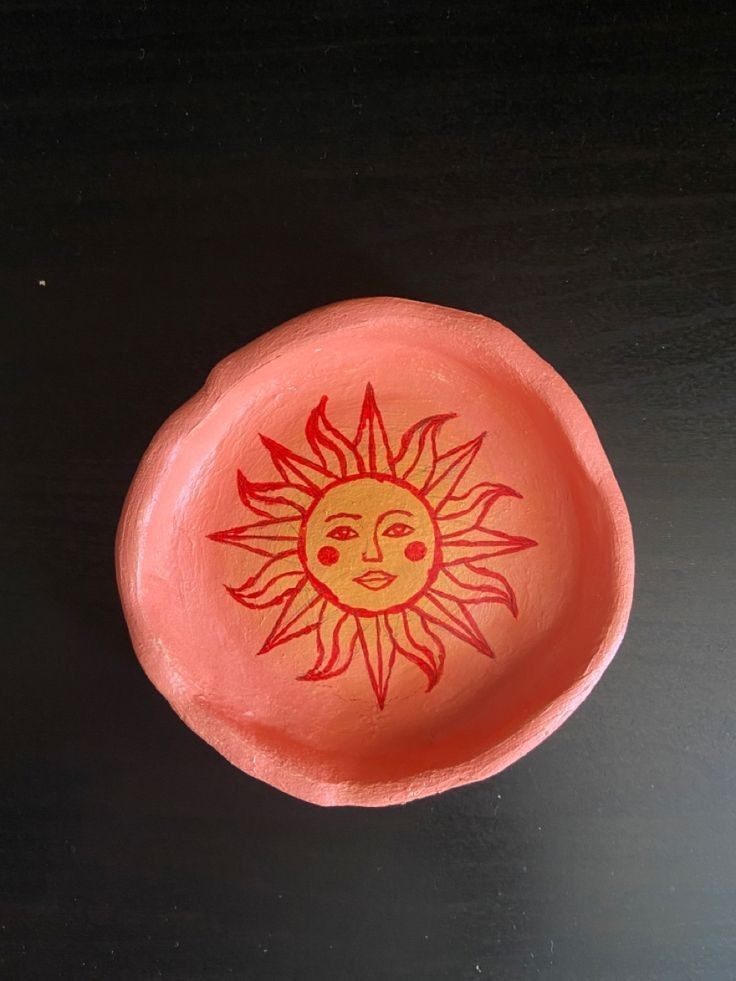 an orange and red bowl with a sun painted on the side, sitting on a black surface