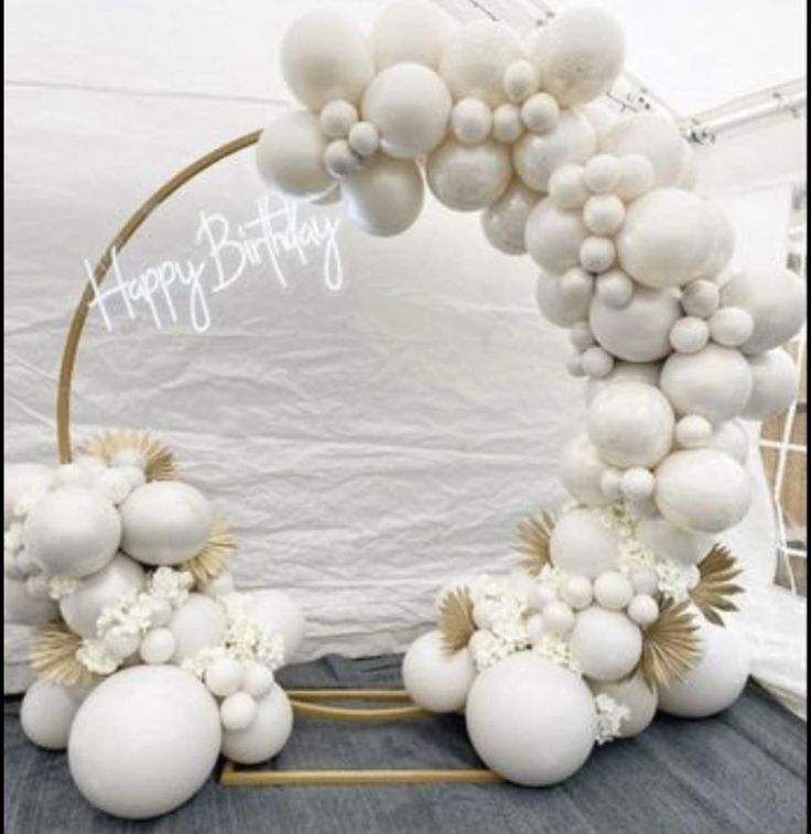 an arch made out of balloons and white flowers is displayed in front of a backdrop