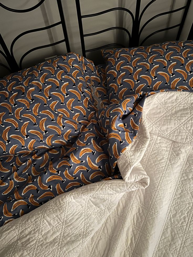 an unmade bed with white sheets and blue and orange comforter on top of it