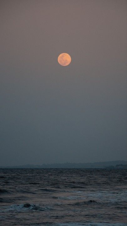 the full moon is setting over the ocean