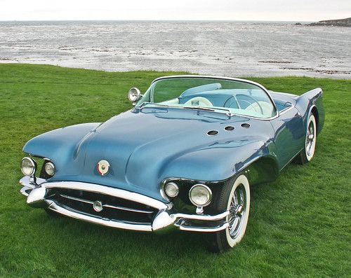 an old car parked in the grass by the water