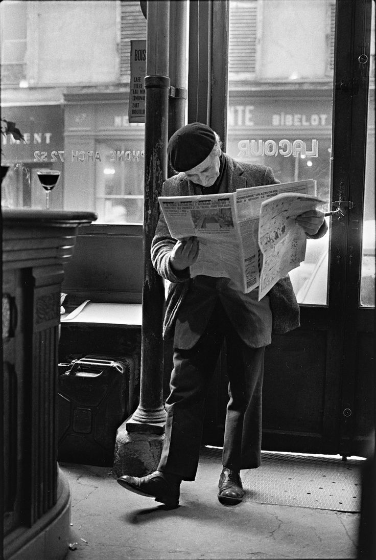 a man reading a newspaper while standing next to a street lamp in front of a building