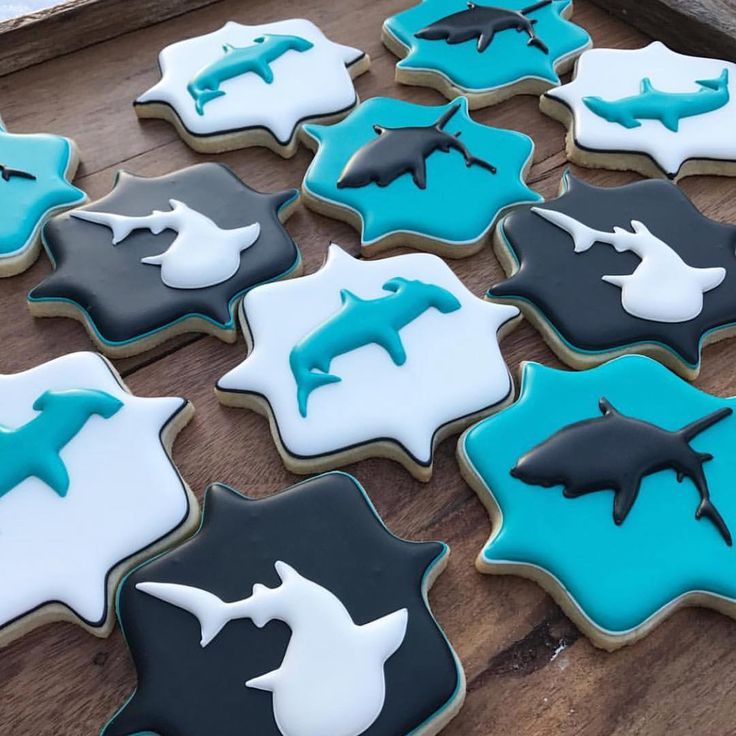 decorated cookies with blue and black icing on a wooden table in the shape of dolphins