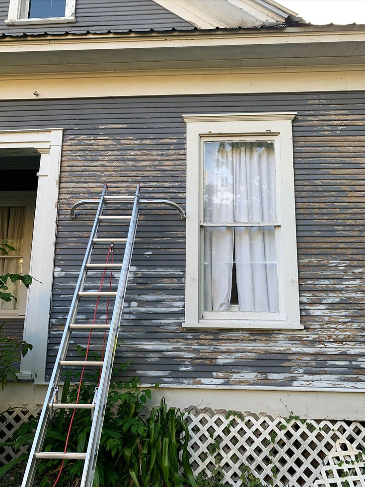 a ladder leaning against the side of a house next to a window with curtains on it