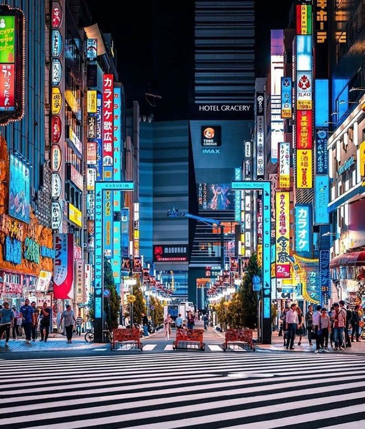 a city street filled with lots of neon signs and people walking across the crosswalk