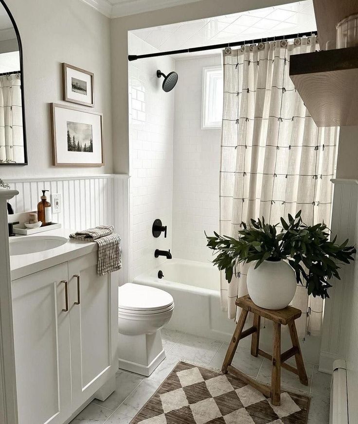 a white bathroom with a checkered rug and potted plant on the stool next to the toilet