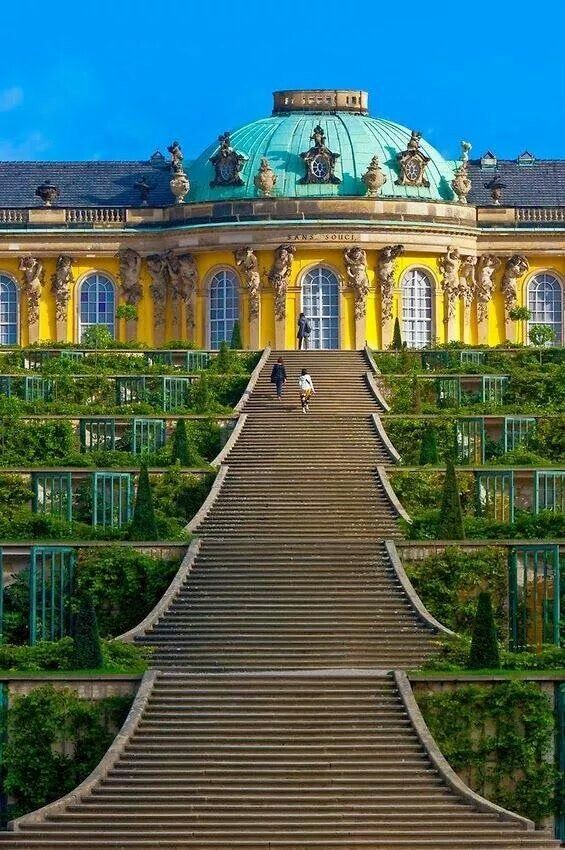 a large building with many windows and stairs leading up to the top floor, surrounded by greenery