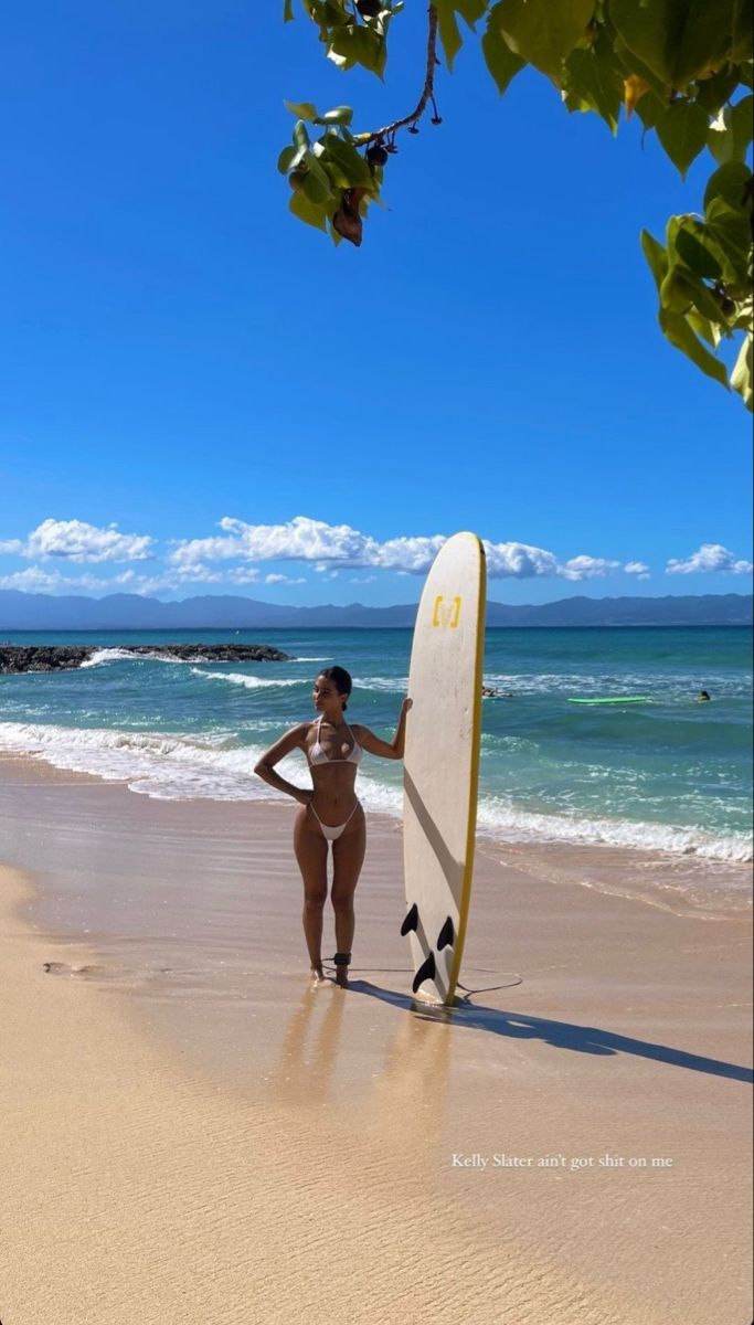 a woman standing on the beach holding a surfboard