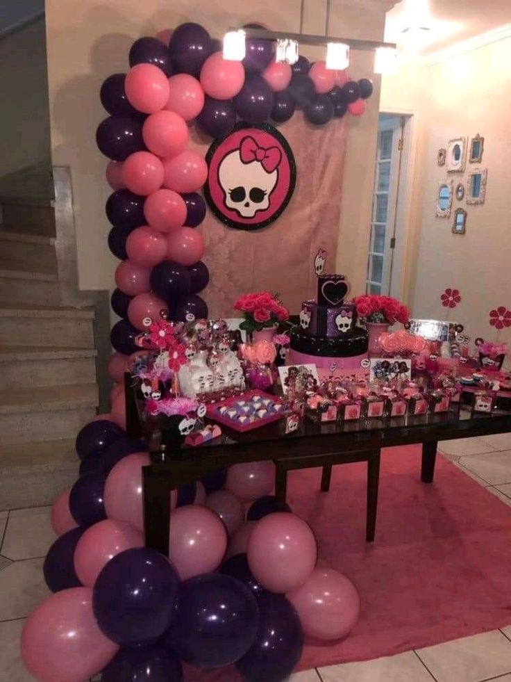 a table topped with lots of balloons next to a pink and purple wallpaper covered in skulls