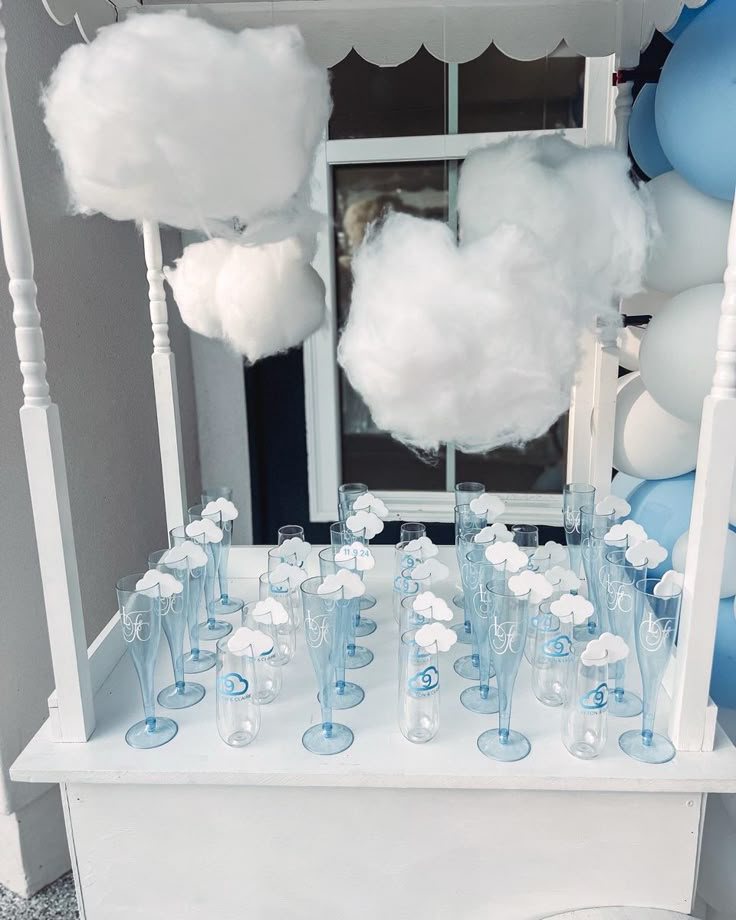 a table topped with lots of glasses filled with water and white fluffy clouds in front of a mirror