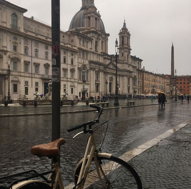 a bike parked on the side of a wet street next to tall buildings with towers