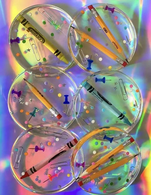 four clear plastic objects with colored dots and pencils in them on a multicolored background