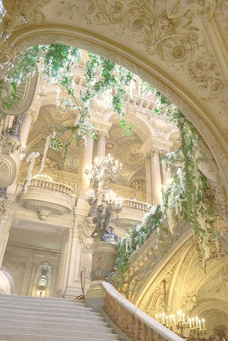 an ornate staircase with chandeliers and greenery on the ceiling