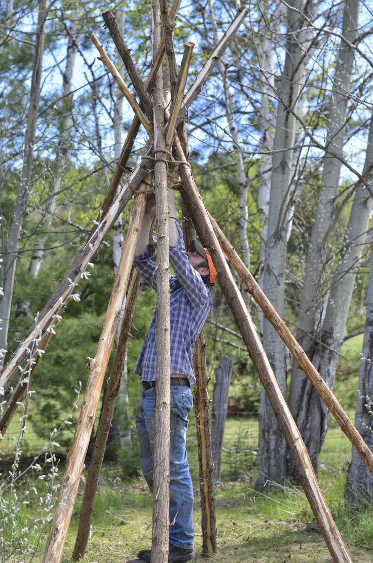 a man building a teepee in the woods