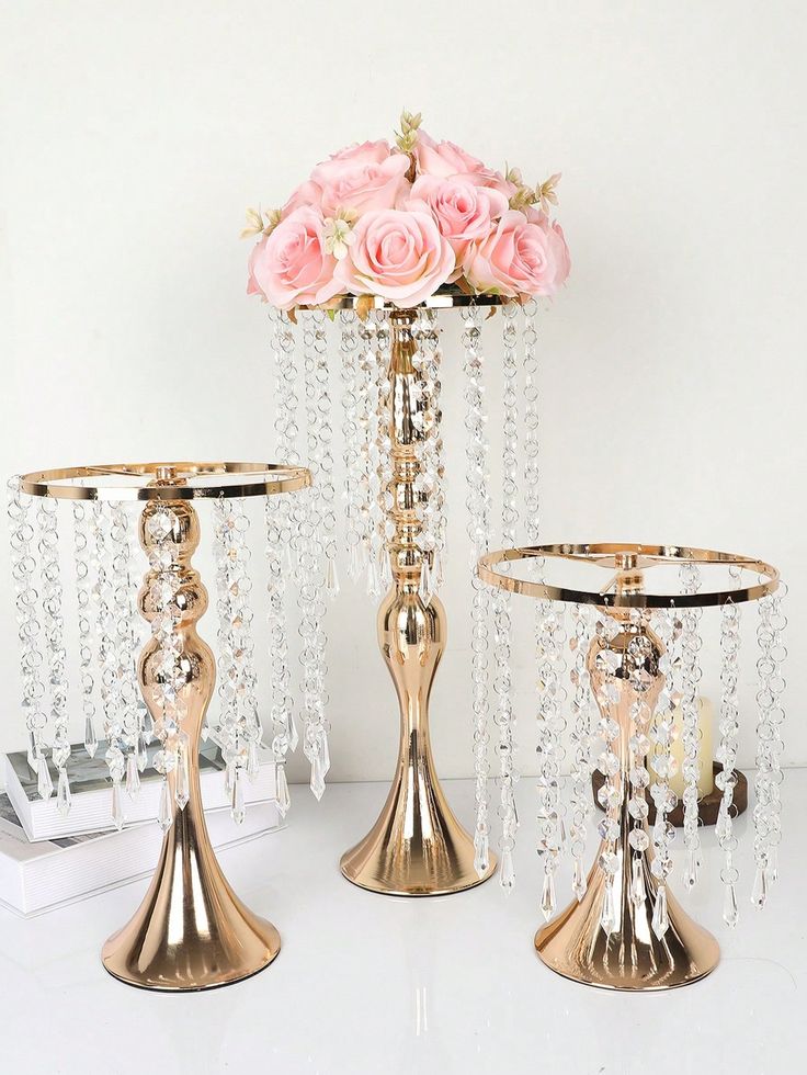 three gold candlesticks with pink roses in the center and two other candle holders