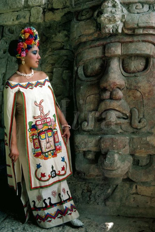 a woman standing next to a stone statue wearing a white dress and headdress