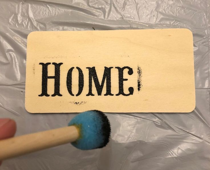 a hand holding a paintbrush with the word home painted on it next to a sign