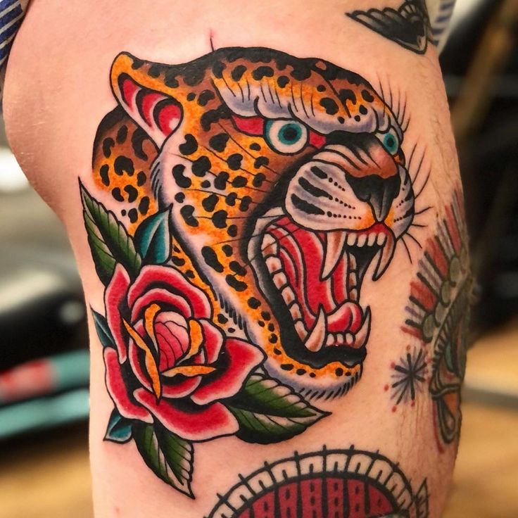 a tattoo on the leg of a man with a leopard and roses in his mouth