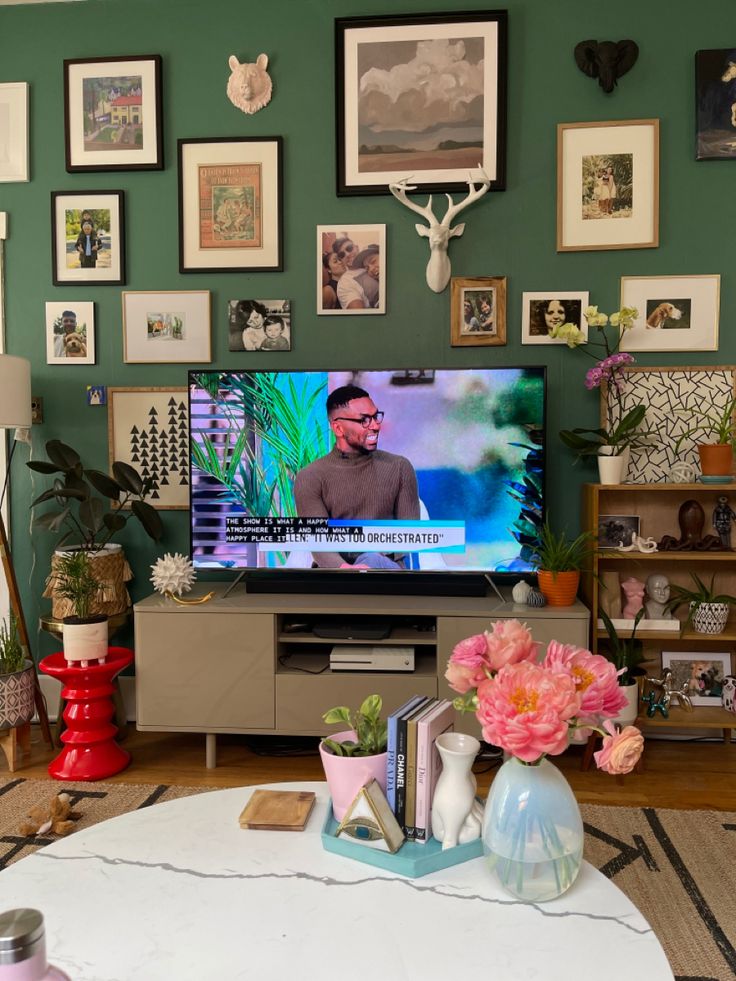 a flat screen tv sitting on top of a wooden table next to a vase filled with flowers