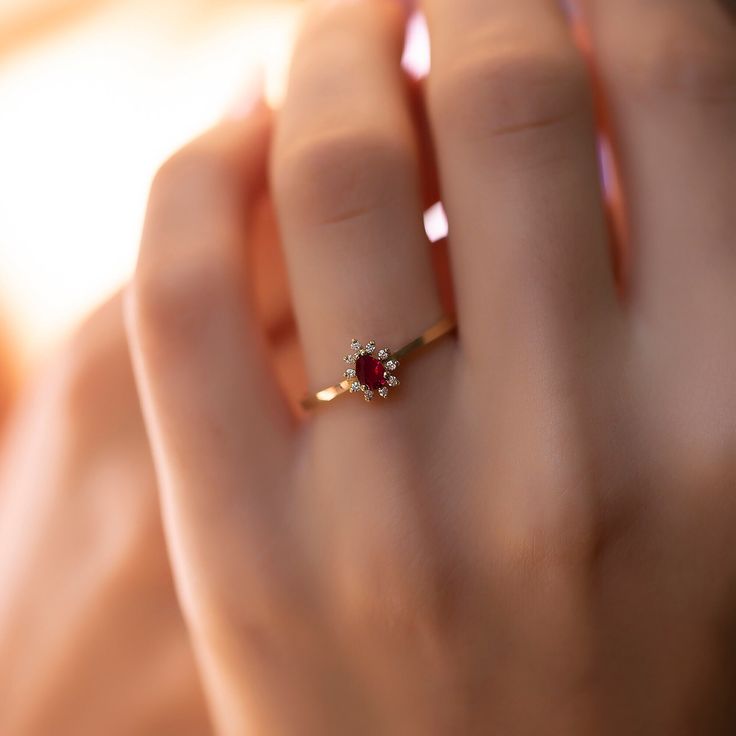 a woman's hand holding a ring with a red stone in the middle and a yellow band around it