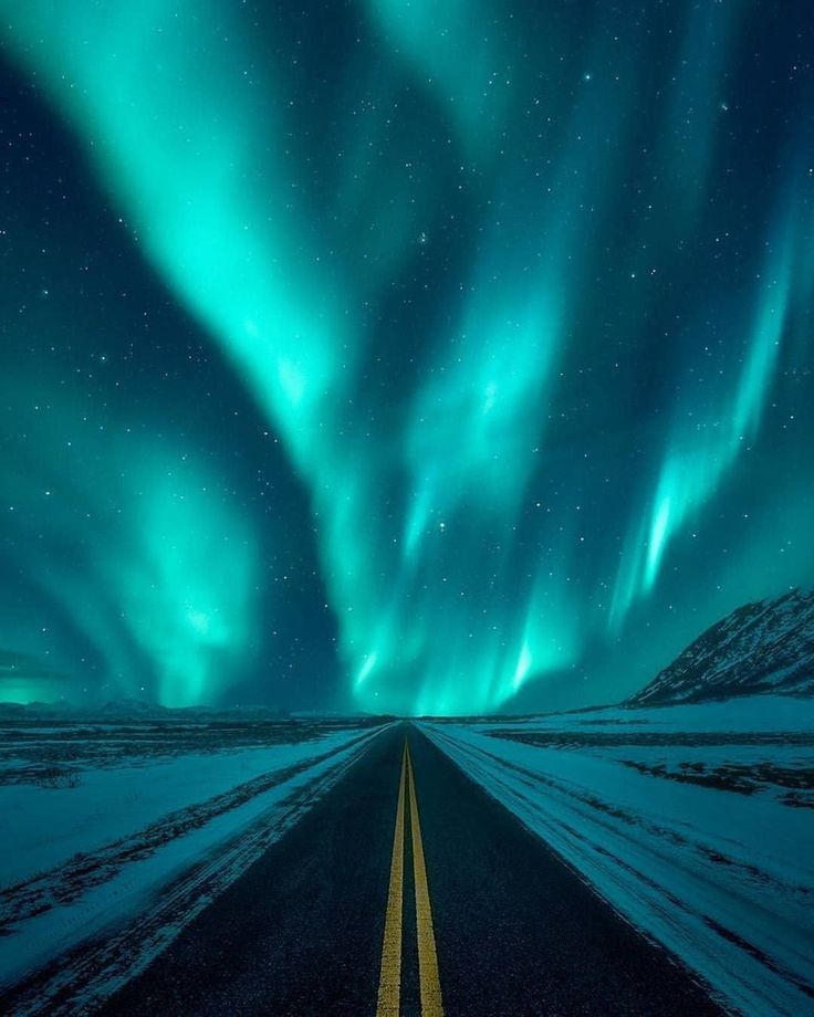 an empty road with the aurora lights in the sky