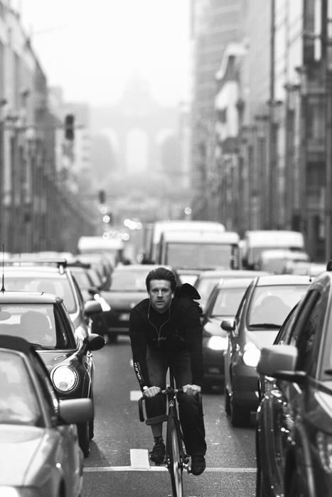 a man riding a bike down a street next to lots of parked cars and tall buildings