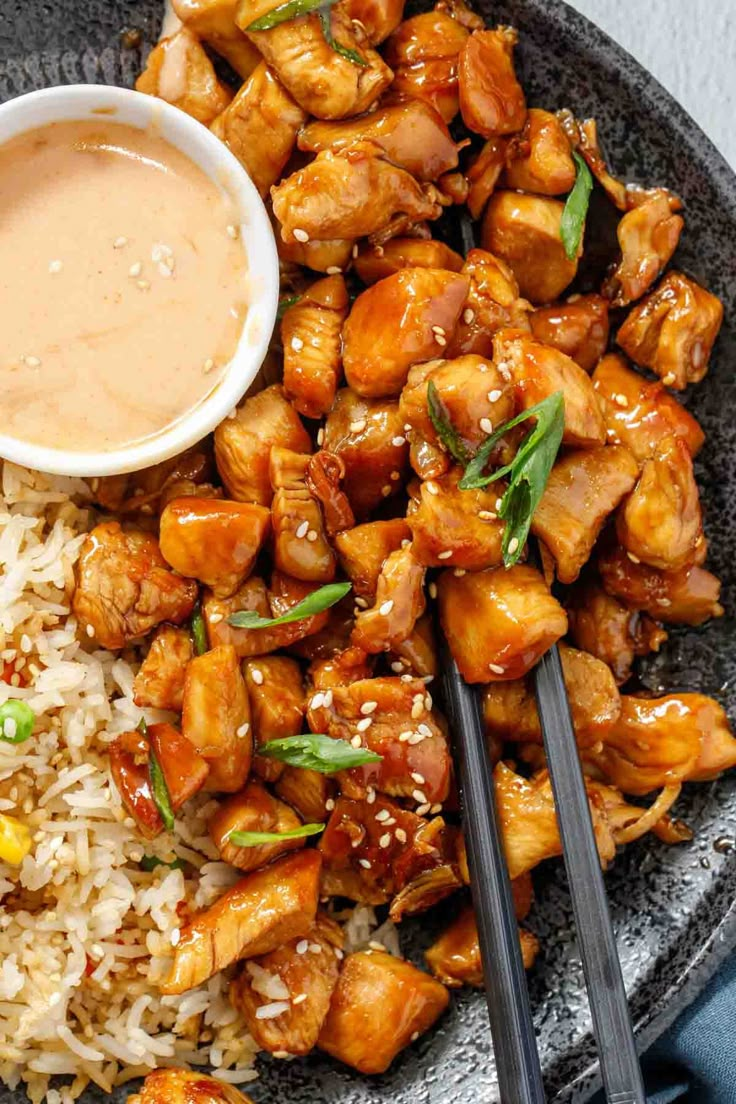 a plate with rice, chicken and sauce next to chopsticks on the side