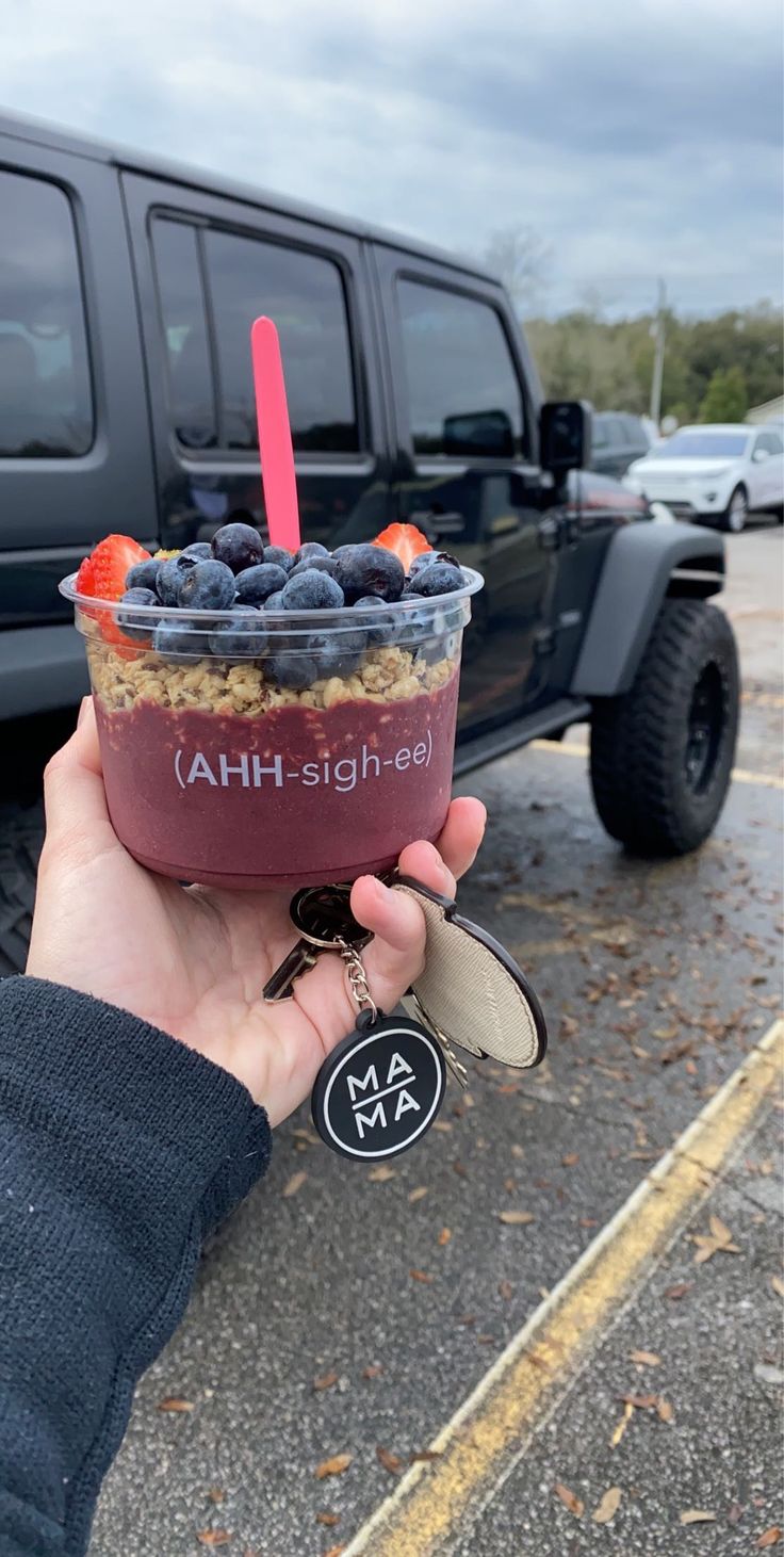 a person holding up a drink in front of a truck with blueberries and strawberries on it