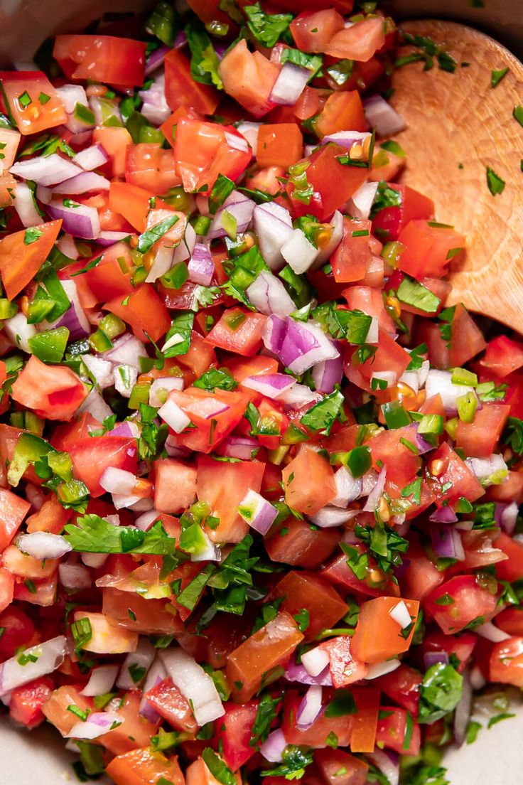 a wooden spoon in a bowl filled with chopped up tomatoes and onions, garnished with cilantro