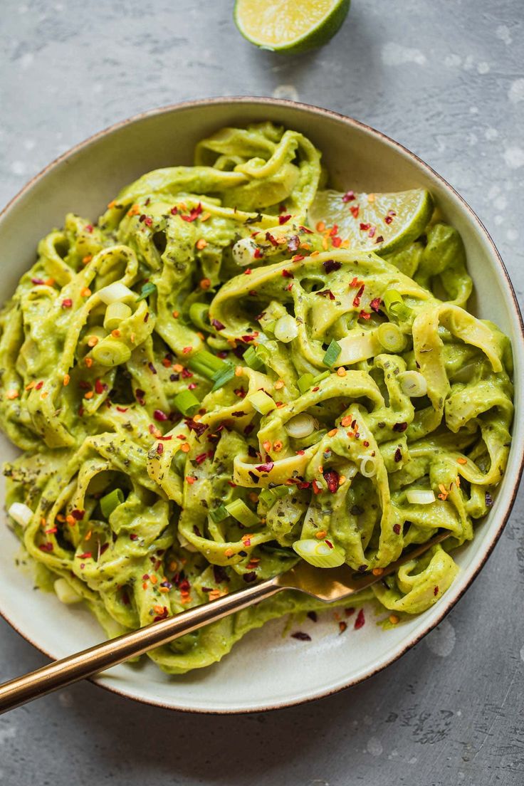 a white bowl filled with green pasta next to a lime slice