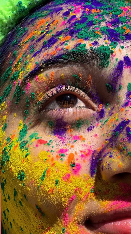 a woman's face covered in colorful powders and green hair, with her eyes closed