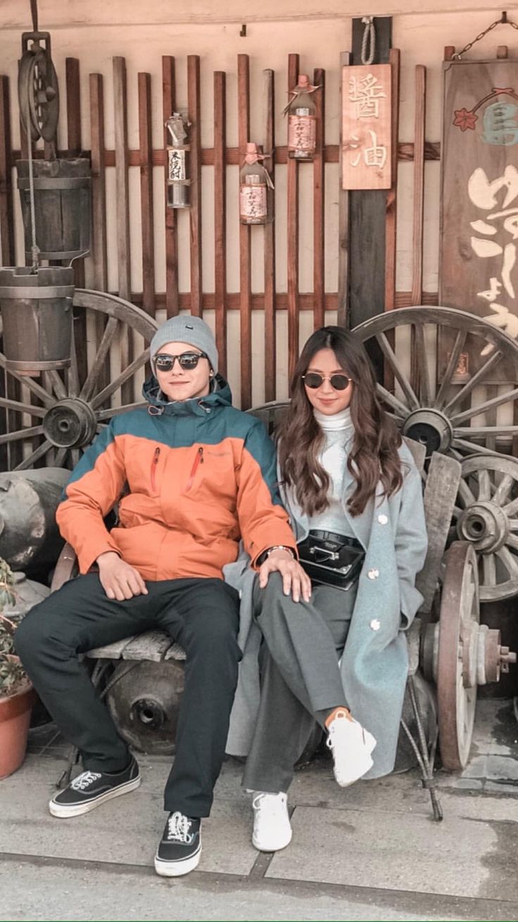 two people sitting on a bench in front of a building with wooden slatted doors