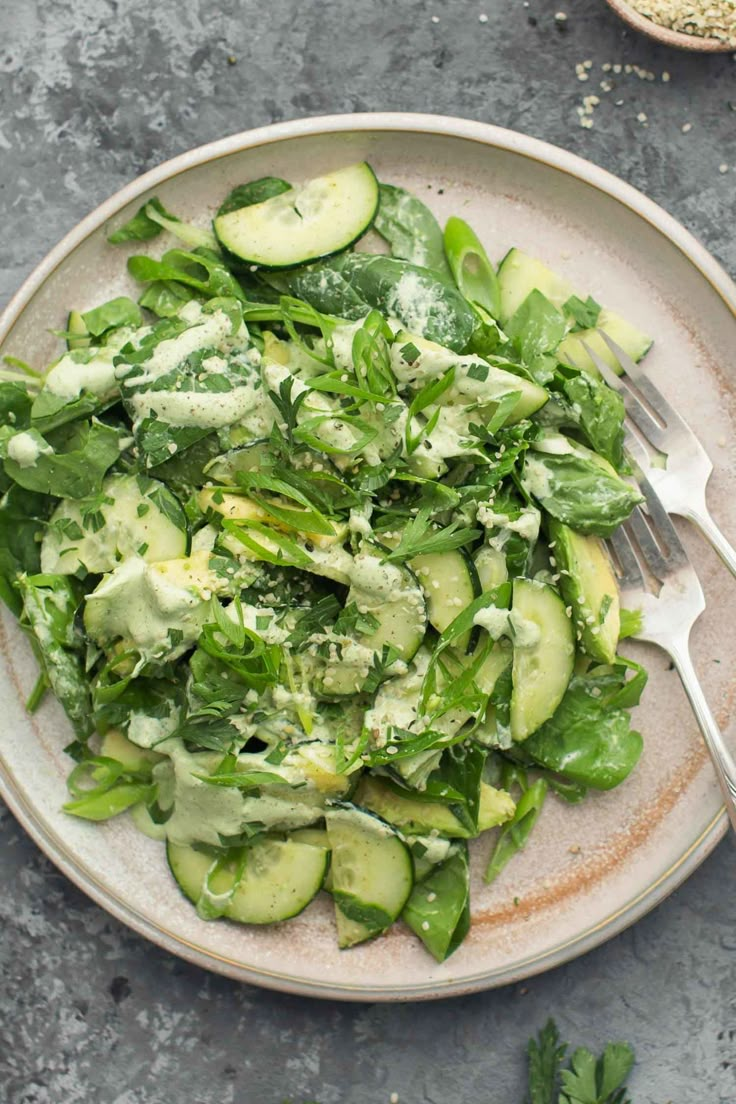 a white plate topped with cucumbers and greens next to a fork on a table