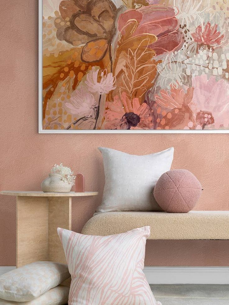 a painting hanging on the wall above a bench with two pillows and a pink pillow