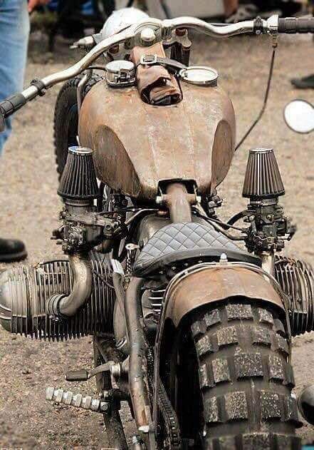 an old rusty motorcycle parked on the side of the road with people in the background