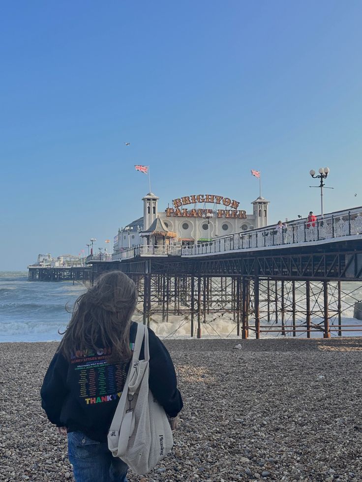 a woman is walking on the beach with her back to the camera and looking at the pier