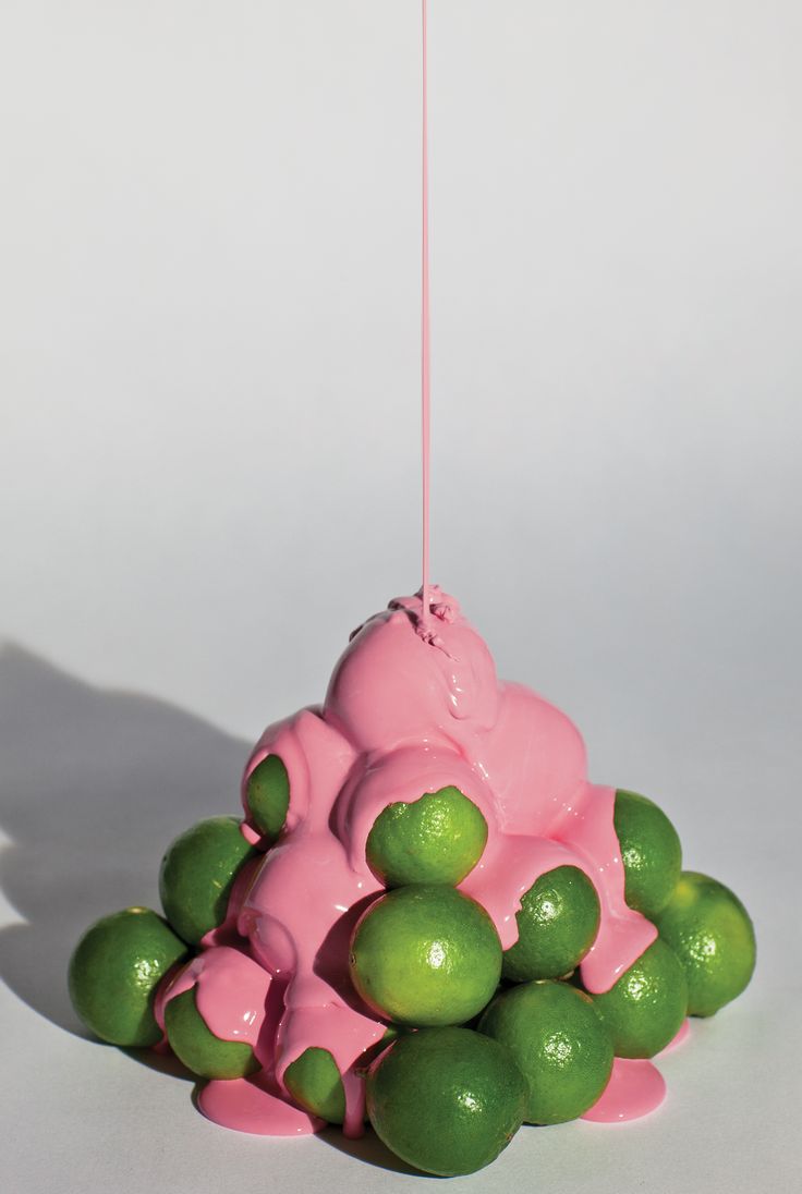 a pink and green sculpture sitting on top of limes in front of a white wall