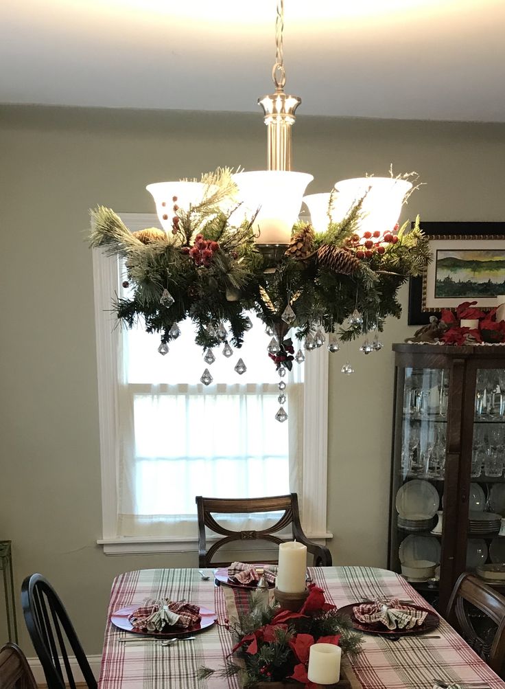 a dining room table decorated for christmas with greenery and candles on it, next to a window