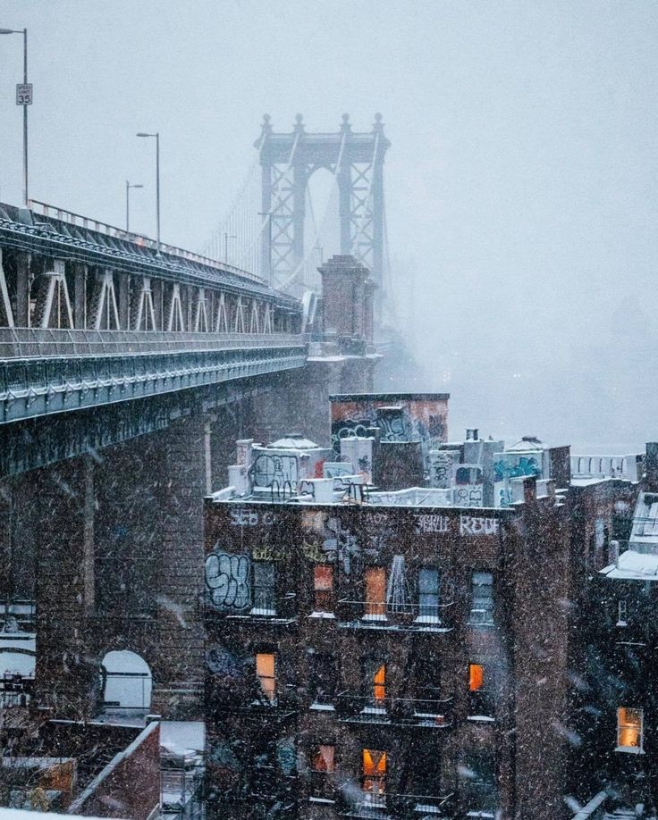 snow falls on the rooftops and buildings in front of a bridge