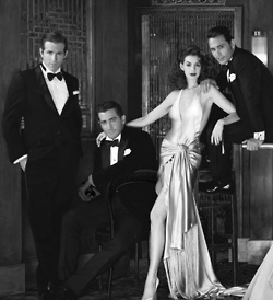 three men and a woman in formal wear posing for a photo with one man wearing a tuxedo