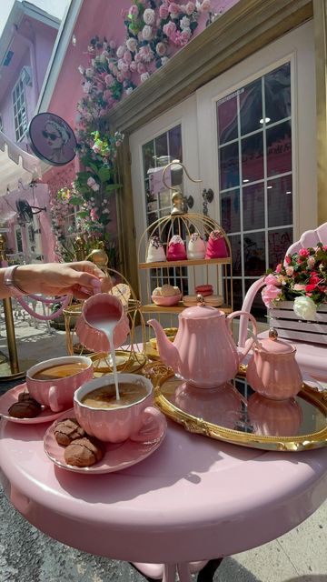 a pink table topped with lots of cups and saucers filled with food next to a building